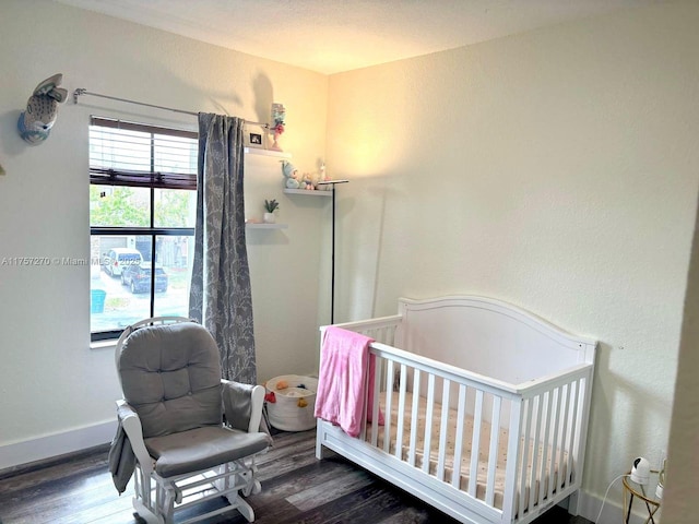 bedroom featuring a nursery area, baseboards, and wood finished floors