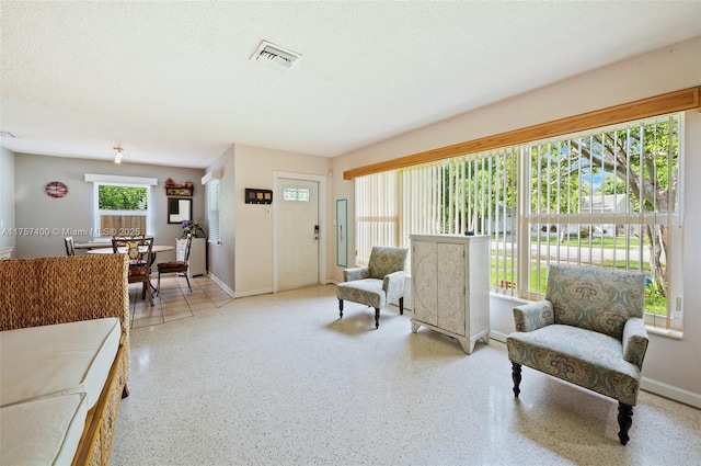 living area featuring a textured ceiling, speckled floor, visible vents, and baseboards