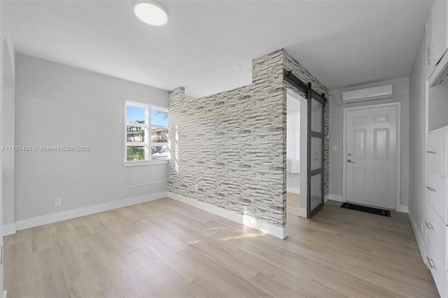 empty room featuring a wall mounted air conditioner, light wood-style flooring, baseboards, and a barn door