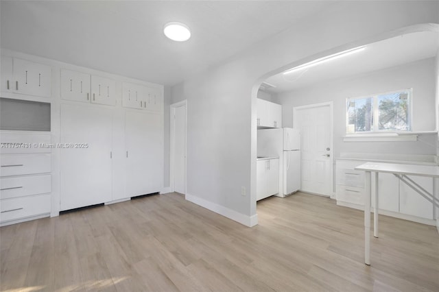 unfurnished bedroom featuring arched walkways, light wood-style flooring, freestanding refrigerator, and baseboards