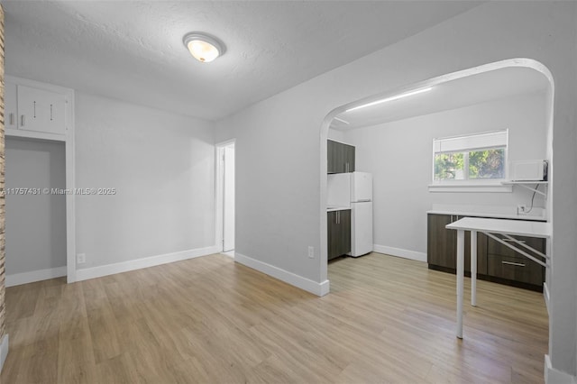 interior space featuring arched walkways, a textured ceiling, light wood-type flooring, and baseboards