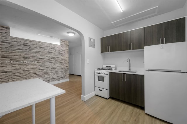 kitchen featuring dark brown cabinetry, white appliances, arched walkways, light countertops, and a sink