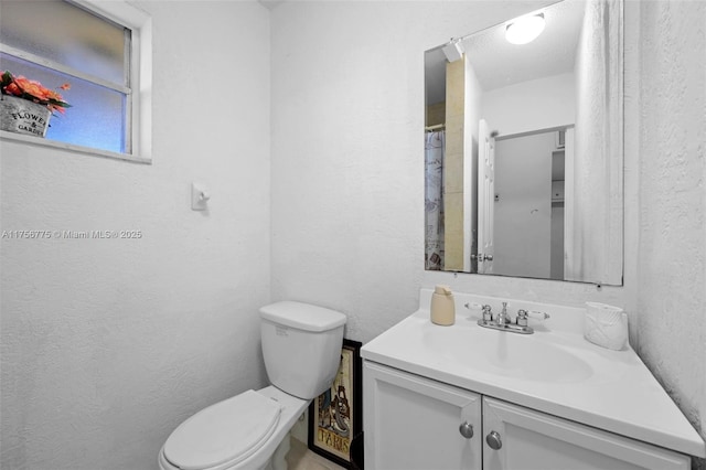 full bath featuring toilet, vanity, and a textured wall