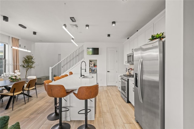 kitchen featuring wood finish floors, stainless steel appliances, light countertops, a sink, and an island with sink