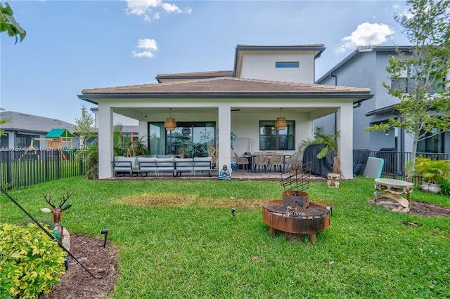 back of property featuring stucco siding, fence, a lawn, and an outdoor living space with a fire pit