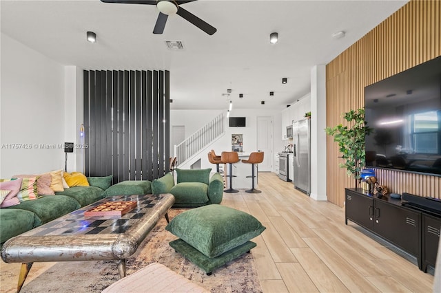 living room with light wood-type flooring, visible vents, stairway, and a ceiling fan