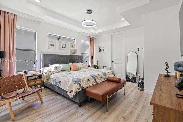 bedroom with a tray ceiling, light wood-style flooring, baseboards, and recessed lighting