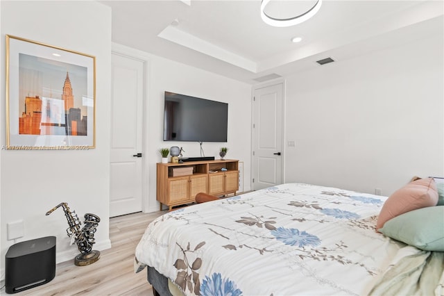 bedroom with light wood-type flooring, visible vents, a tray ceiling, and recessed lighting