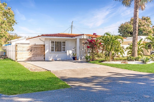 view of front of home featuring fence, a front yard, a tile roof, and stucco siding