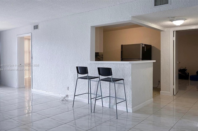 kitchen featuring a textured ceiling, a textured wall, visible vents, and freestanding refrigerator