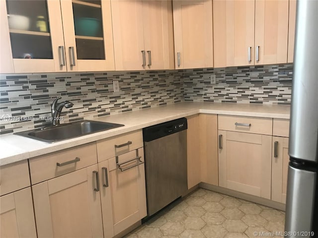 kitchen featuring decorative backsplash, glass insert cabinets, stainless steel appliances, light countertops, and a sink