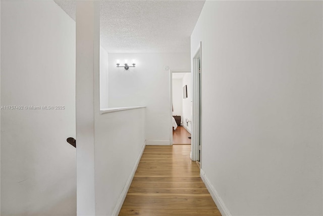 hallway with light wood-style floors, an upstairs landing, a textured ceiling, and baseboards