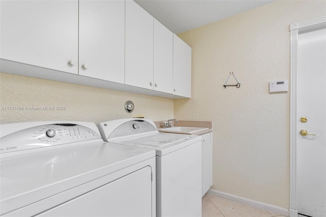 laundry room featuring cabinet space, light tile patterned floors, baseboards, washing machine and clothes dryer, and a sink