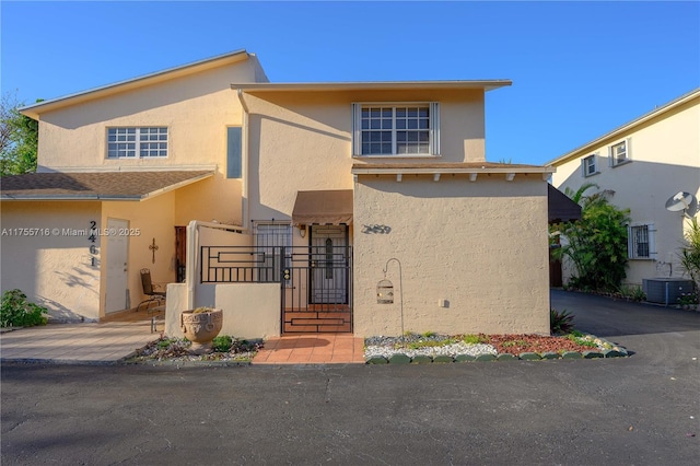 view of front of house featuring driveway, central air condition unit, a gate, and stucco siding