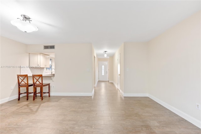 unfurnished room with visible vents, a sink, light wood-style flooring, and baseboards