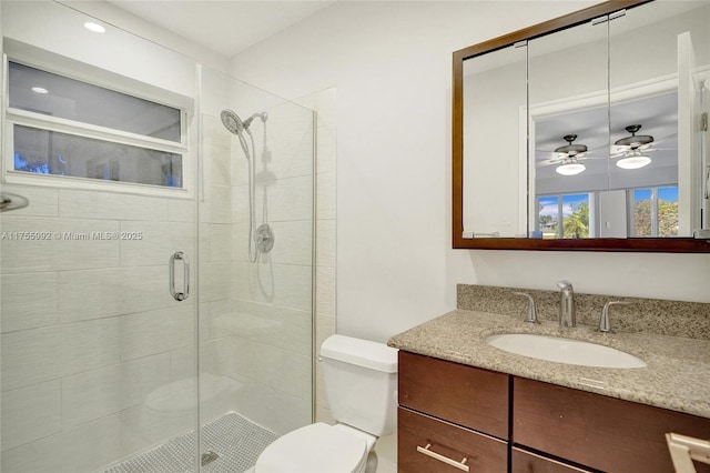 bathroom featuring toilet, a stall shower, vanity, and a ceiling fan