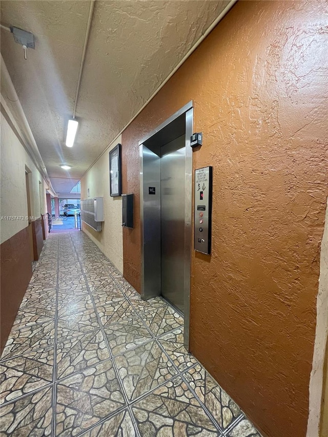 corridor with a textured ceiling, a textured wall, elevator, and stone finish flooring