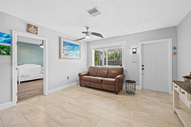 living area with ceiling fan, a textured ceiling, visible vents, and baseboards