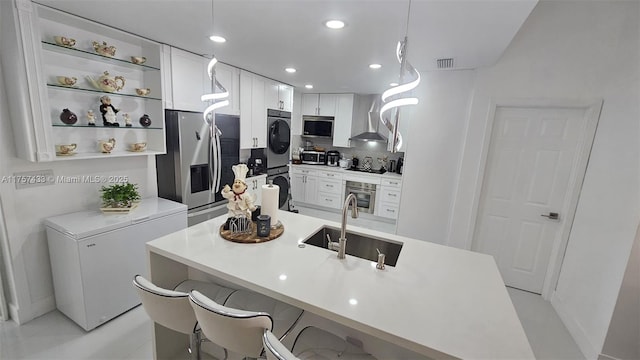 kitchen with visible vents, wall chimney range hood, stainless steel appliances, white cabinetry, and a sink