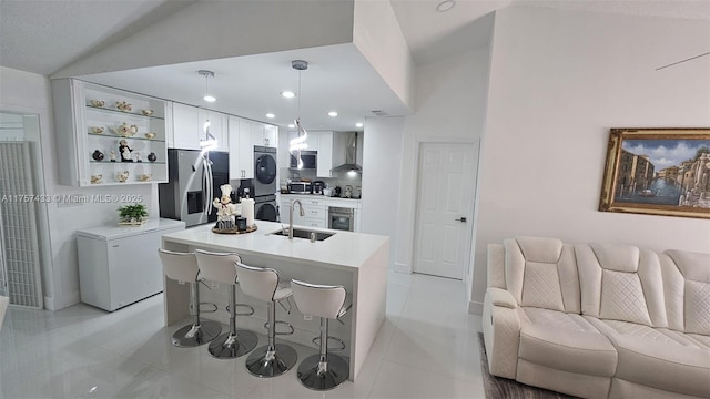 kitchen with wall chimney range hood, open floor plan, a kitchen bar, stainless steel appliances, and a sink