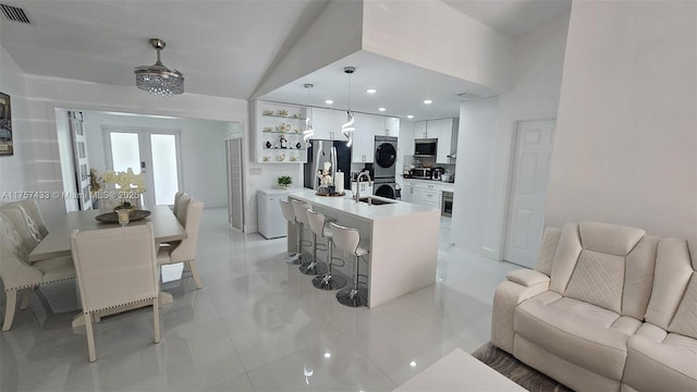 kitchen featuring visible vents, a sink, white cabinetry, stacked washing maching and dryer, and stainless steel appliances