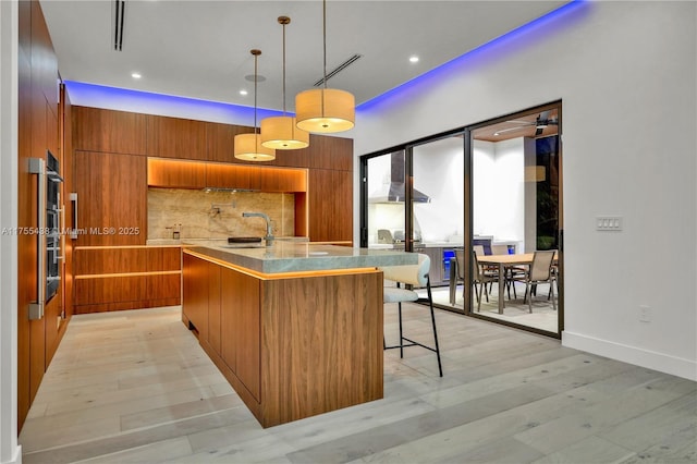 kitchen featuring decorative backsplash, modern cabinets, brown cabinets, light wood-style floors, and a sink