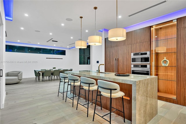 kitchen featuring stainless steel double oven, brown cabinets, a sink, and modern cabinets