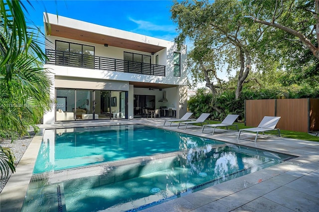 back of property featuring a balcony, fence, a pool with connected hot tub, stucco siding, and a patio area