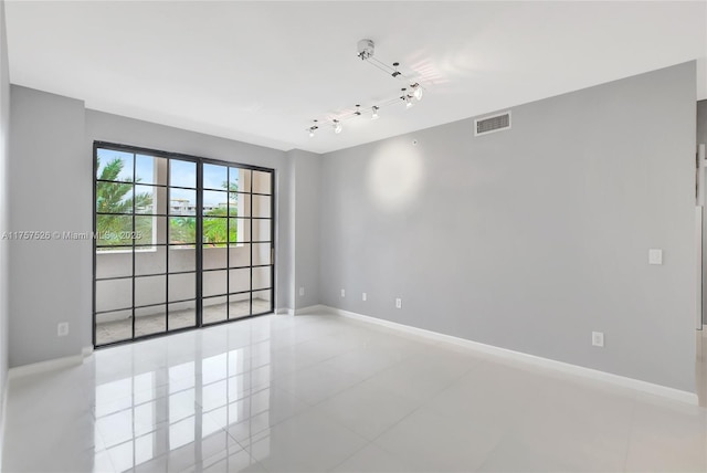 tiled spare room featuring rail lighting, visible vents, and baseboards