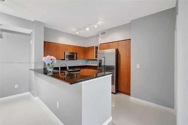 kitchen featuring light tile patterned floors, stainless steel appliances, a peninsula, visible vents, and brown cabinets