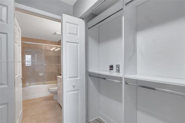 bathroom with bath / shower combo with glass door, toilet, and tile patterned floors