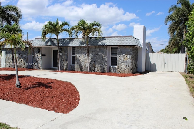 view of front facade featuring driveway, stone siding, a gate, and roof with shingles