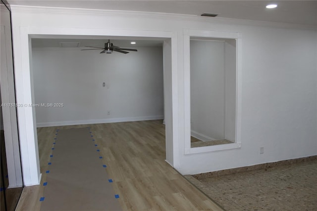 empty room with wood finished floors, visible vents, baseboards, a ceiling fan, and ornamental molding