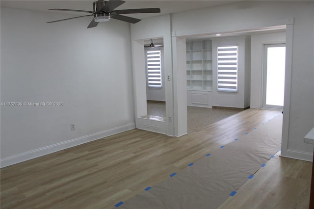 empty room with a ceiling fan, baseboards, and wood finished floors