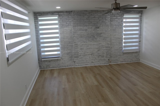 unfurnished room featuring brick wall, plenty of natural light, and wood finished floors