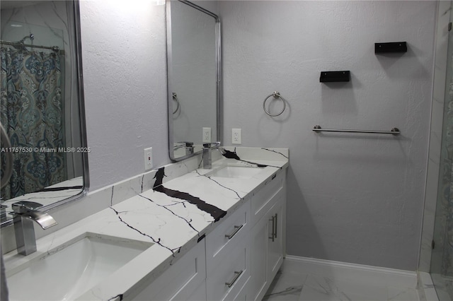 full bath featuring marble finish floor, double vanity, a sink, and baseboards