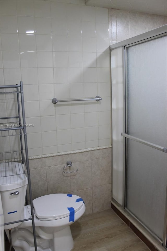 full bathroom featuring wood finished floors, a shower stall, toilet, and tile walls