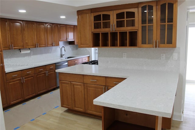 kitchen featuring light countertops, glass insert cabinets, a sink, dishwasher, and a peninsula