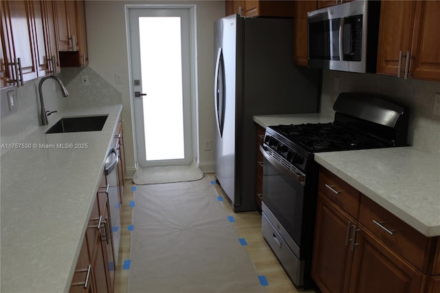 kitchen with stainless steel appliances, light countertops, decorative backsplash, a sink, and light wood-type flooring