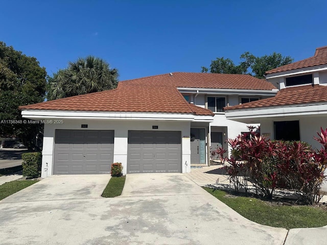 mediterranean / spanish home featuring a tiled roof, stucco siding, an attached garage, and driveway