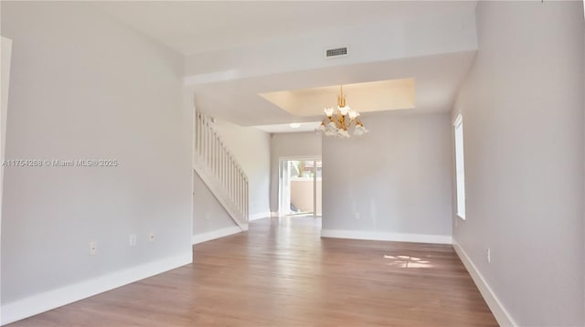 empty room featuring a raised ceiling, visible vents, an inviting chandelier, wood finished floors, and baseboards