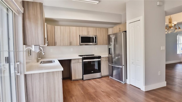 kitchen featuring light countertops, stainless steel appliances, light brown cabinetry, light wood-style floors, and a sink