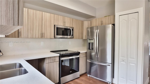 kitchen with light countertops, light brown cabinetry, appliances with stainless steel finishes, a sink, and modern cabinets