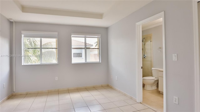 empty room featuring a tray ceiling, baseboards, and light tile patterned floors