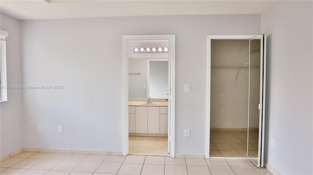 unfurnished bedroom featuring a closet, light tile patterned flooring, a sink, and ensuite bath