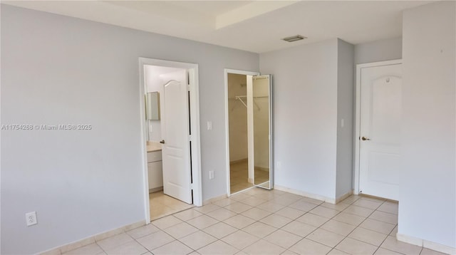 unfurnished bedroom with light tile patterned floors, a closet, visible vents, a spacious closet, and baseboards