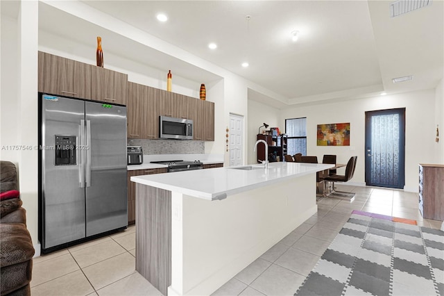 kitchen with stainless steel appliances, tasteful backsplash, light countertops, light tile patterned flooring, and an island with sink