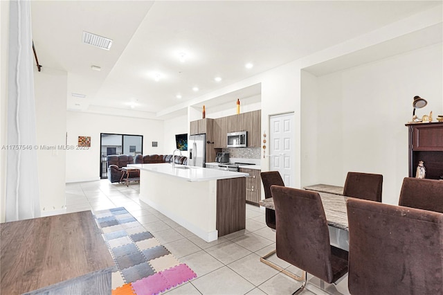 kitchen with visible vents, appliances with stainless steel finishes, open floor plan, a kitchen island with sink, and light countertops