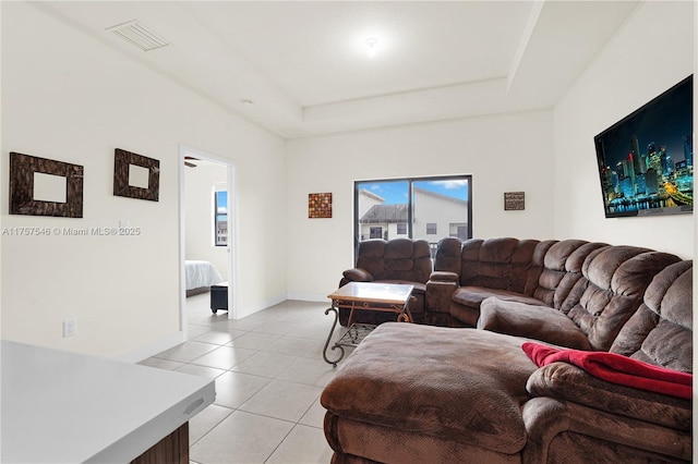 living room with light tile patterned floors, baseboards, visible vents, and a tray ceiling