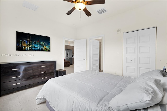 bedroom featuring stainless steel refrigerator with ice dispenser, a closet, visible vents, a ceiling fan, and light tile patterned flooring